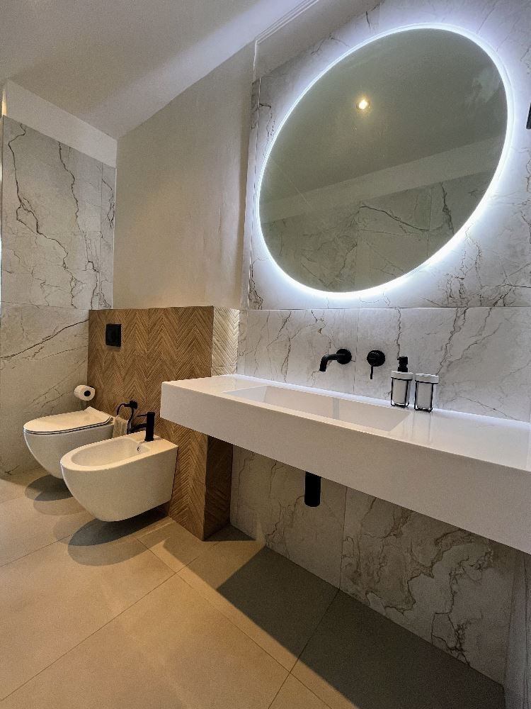 Bagno moderno ristrutturato da Keproject con rivestimenti effetto marmo e specchio retroilluminato